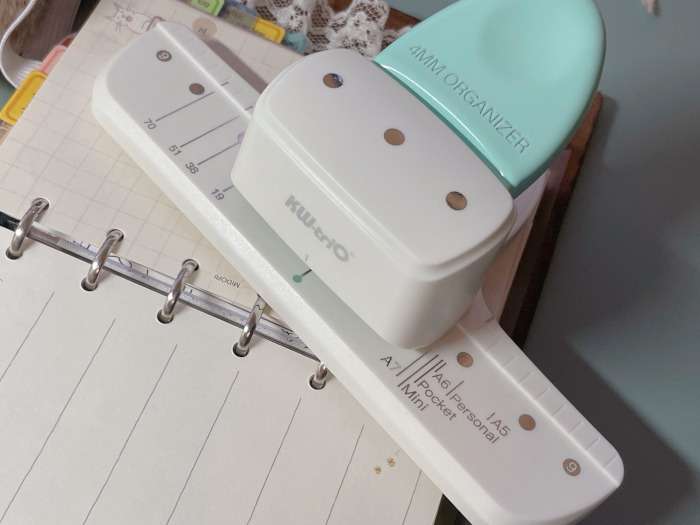 A 6-hole puncher with a mint handle labeled "4MM ORGANIZER," positioned on top of a ring binder insert.