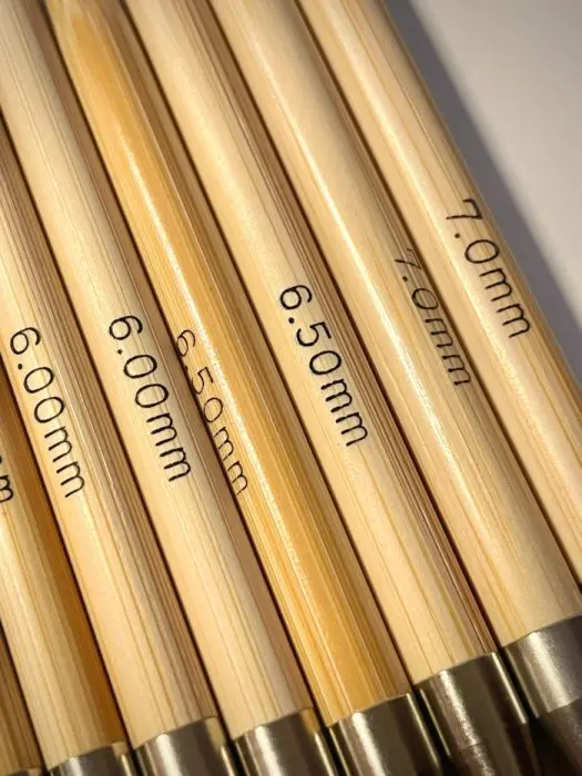 Close-up of two wooden knitting needles with metal connectors and yellow cables attached.