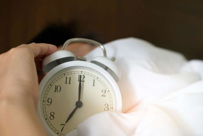 hand turning off a white alarm clock in bed during early morning wake-up