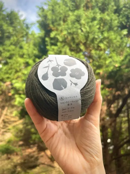 Daruma Ramie Cotton yarn ball, dark green color held in hand outdoors with trees in background