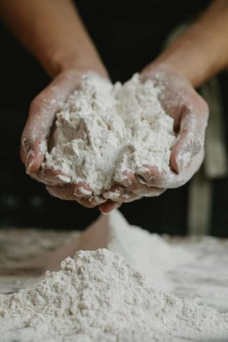 Person holding flour in hands preparing dough