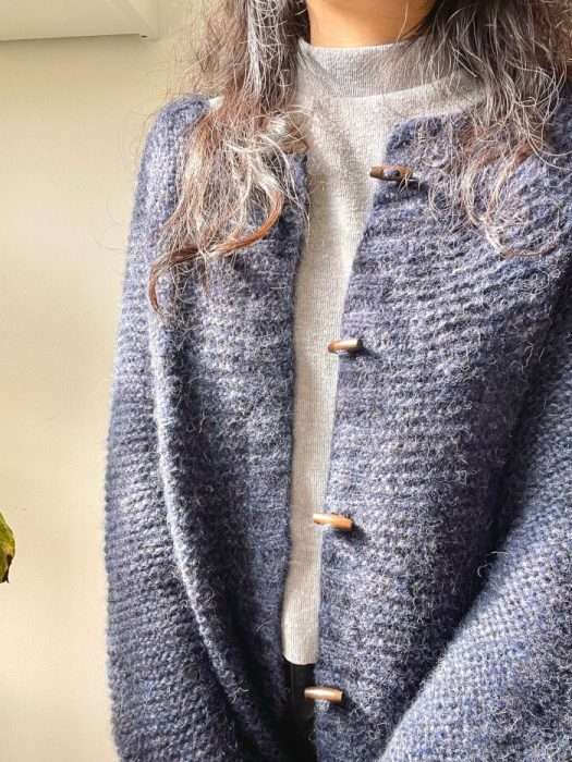 Upper-body view of a person wearing the knitted Kiki cardigan with wooden buttons on the front