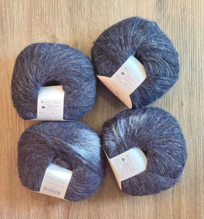 four skeins of KnitPicks Wonderfluff. They are deep navy fuzzy yarn arranged on a wooden surface