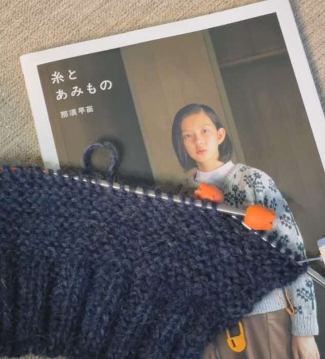 navy cardigan knitting in progress on needles with orange stoppers placed over a Japanese knitting book cover