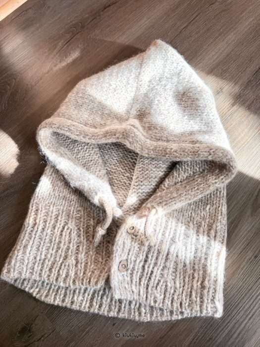 Finished knit balaclava folded flat, aran-weight texture with ties visible