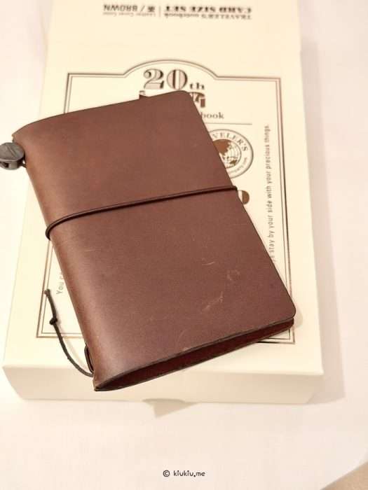 Close-up of the Traveler's Notebook 20th Anniversary brown leather card size cover resting on the limited edition packaging box